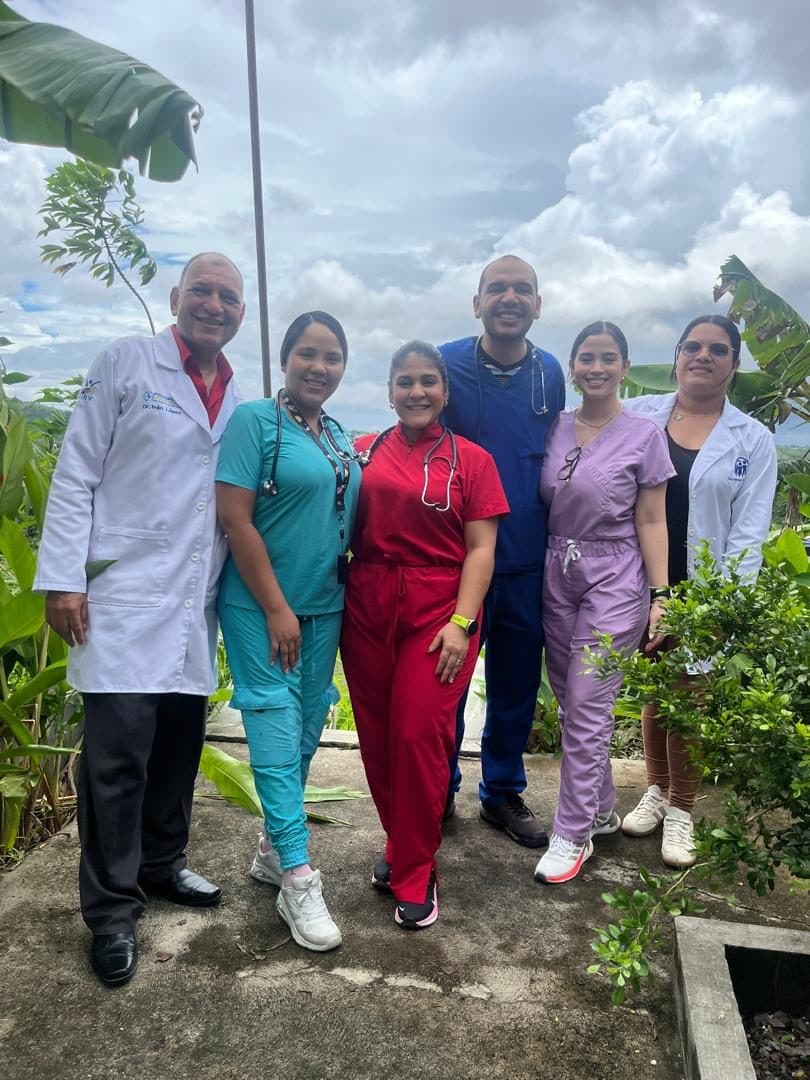 El Dr. Iván López de bata blanca junto a un equipo de médicos y enfermeras con uniformes de colores, al aire libre